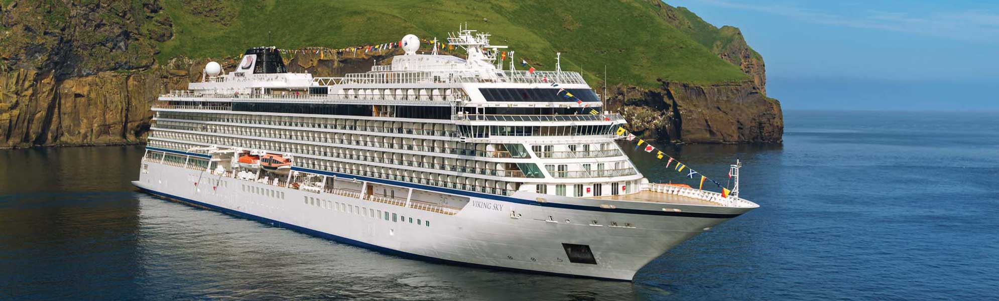 The Viking Sky, a modern luxury cruise ship, is anchored in a dramatic Norwegian fjord surrounded