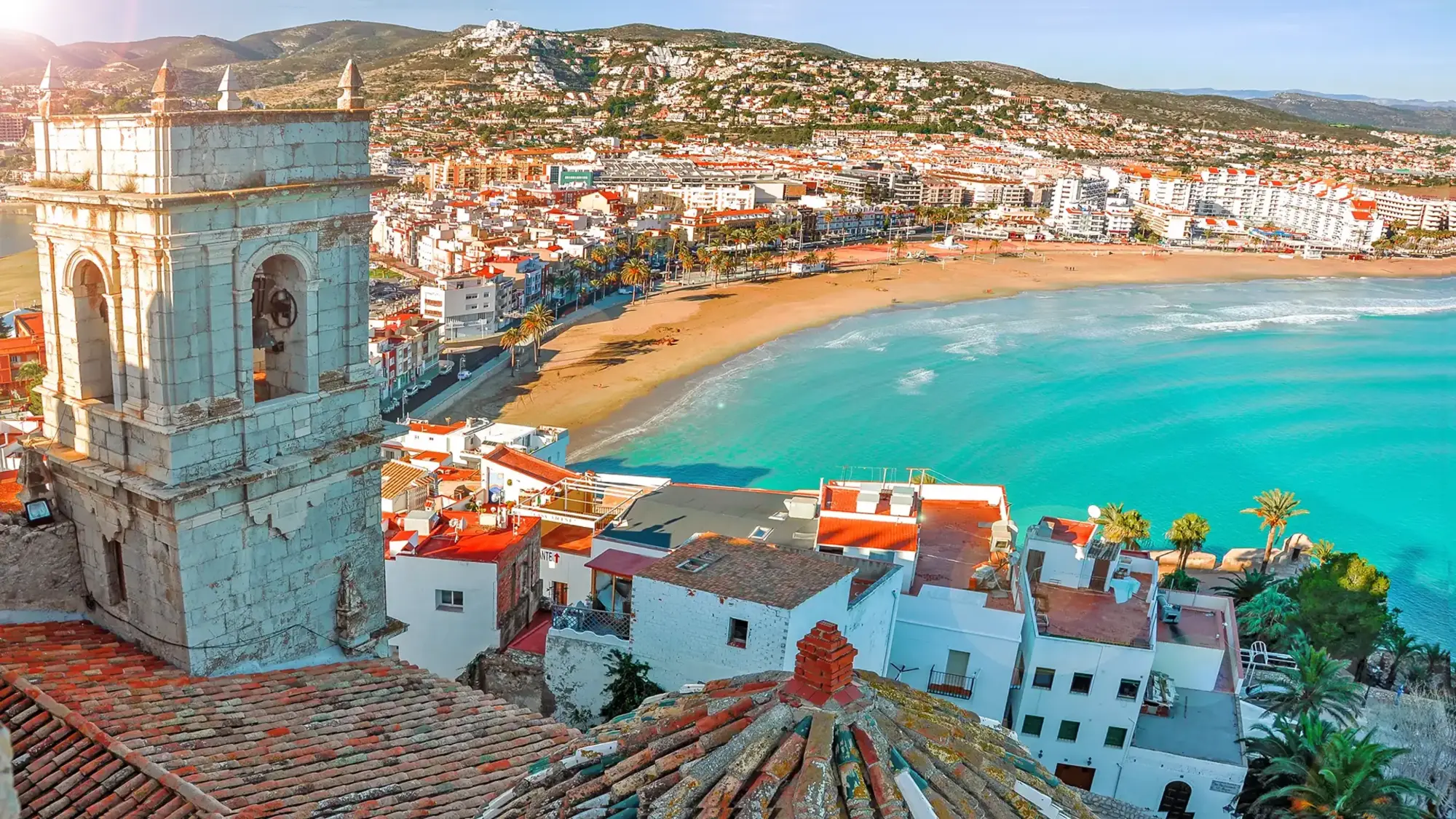 Coastal Beach Town with Historic Tower and Turquoise Waters A picturesque Mediterranean coastal town featuring a distinctive turquoise-tiled historic tower
