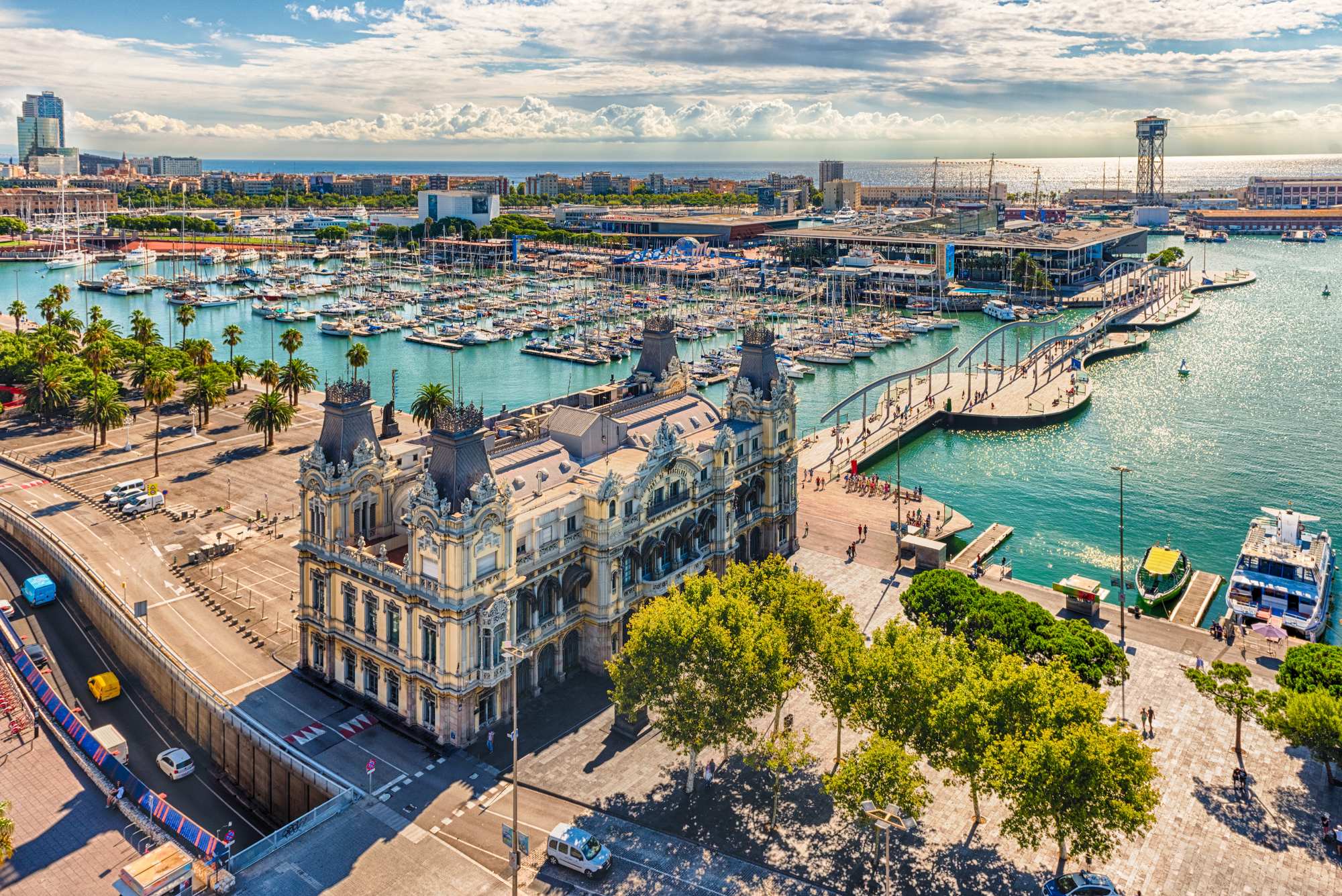 An expansive aerial view of Barcelona's Port Vell waterfront district, featuring the iconic