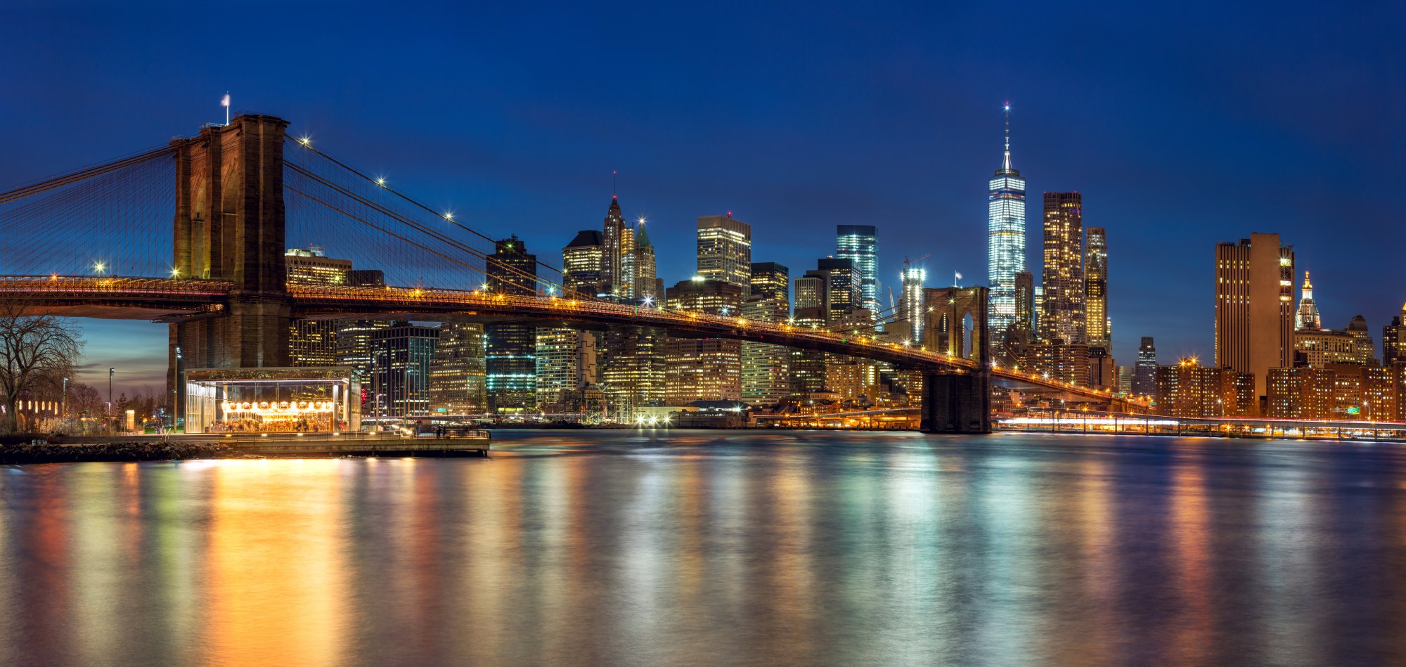 An iconic nighttime view of the illuminated Brooklyn Bridge spanning the East River with