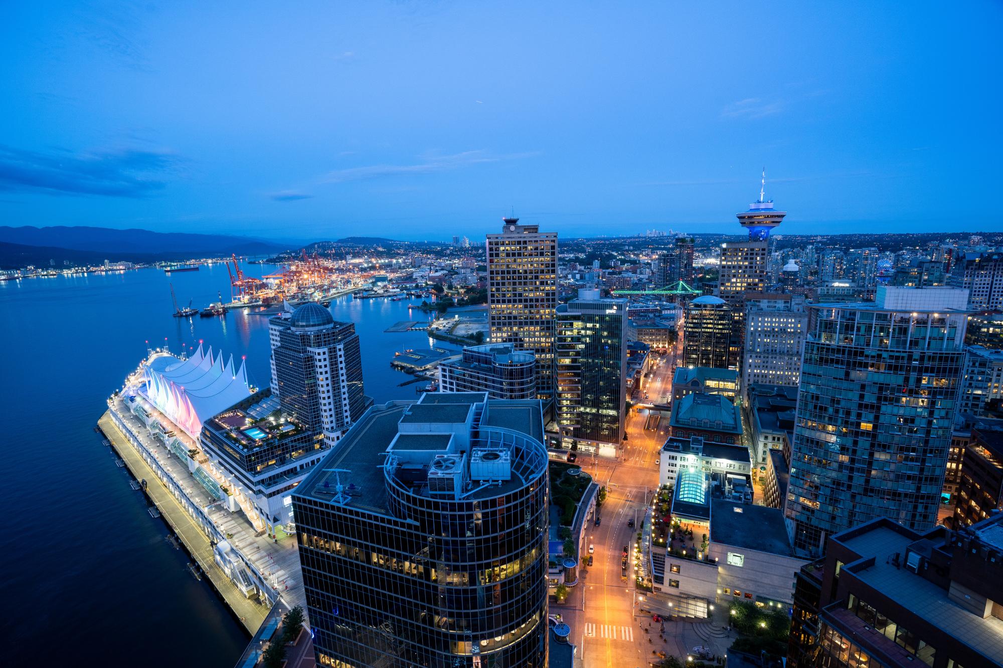A stunning aerial view of downtown Vancouver at dusk, featuring illuminated skyscrapers